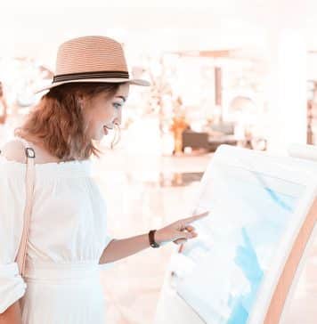 Happy asian girl using an interactive info touchscreen assistant in the shopping Mall.