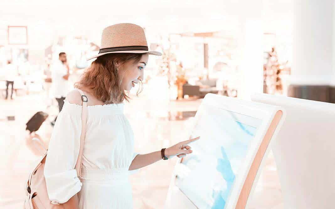 Happy asian girl using an interactive info touchscreen assistant in the shopping Mall.